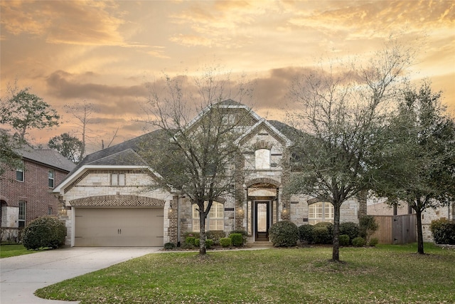 french country style house featuring an attached garage, a front lawn, fence, stone siding, and driveway