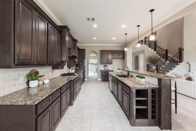 kitchen with visible vents, dark brown cabinetry, stainless steel gas stovetop, arched walkways, and a sink