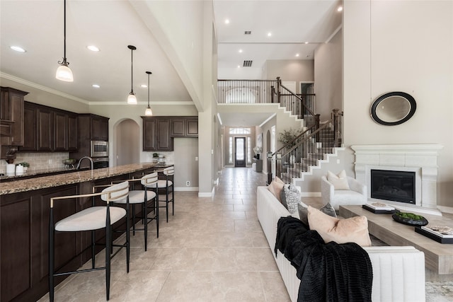 kitchen with light stone counters, backsplash, open floor plan, appliances with stainless steel finishes, and dark brown cabinets