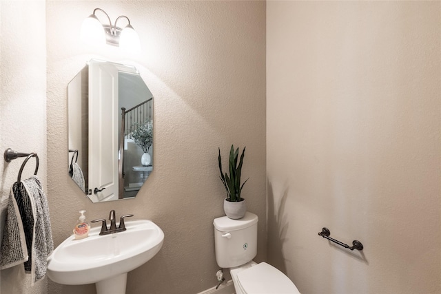 half bathroom with toilet, a textured wall, and a sink