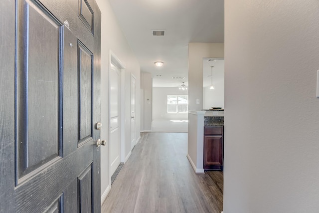 hall featuring visible vents, baseboards, and wood finished floors