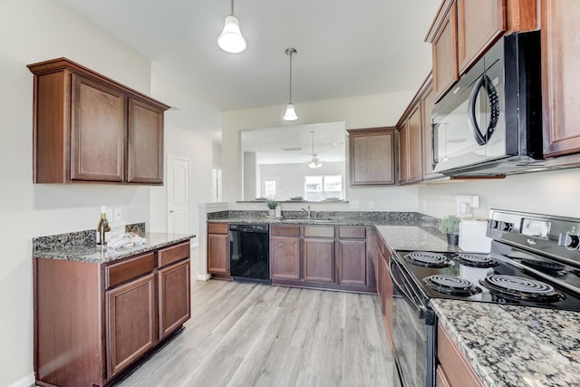 kitchen with light wood-type flooring, black appliances, pendant lighting, light stone counters, and a sink