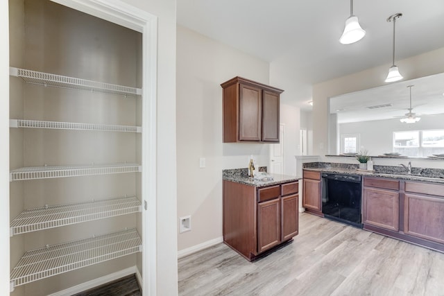 kitchen featuring light wood finished floors, pendant lighting, black dishwasher, stone counters, and a sink