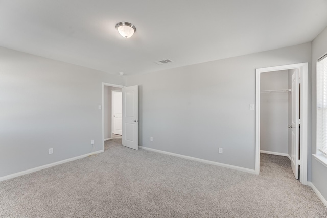 unfurnished bedroom featuring visible vents, baseboards, a closet, light carpet, and a walk in closet