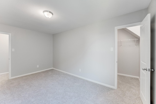 unfurnished bedroom with a closet, carpet flooring, a walk in closet, and baseboards