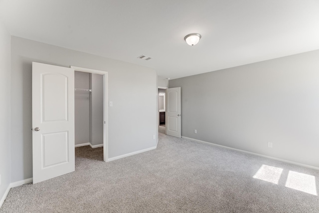 unfurnished bedroom featuring a walk in closet, carpet, visible vents, and baseboards