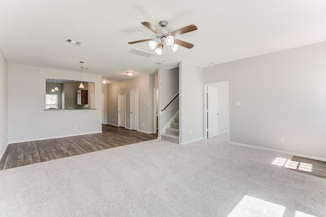 unfurnished living room featuring visible vents, a ceiling fan, dark colored carpet, baseboards, and stairs