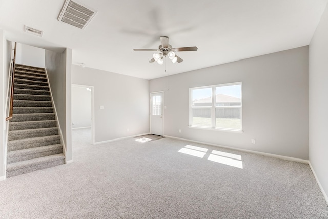 carpeted spare room with stairway, baseboards, visible vents, and ceiling fan