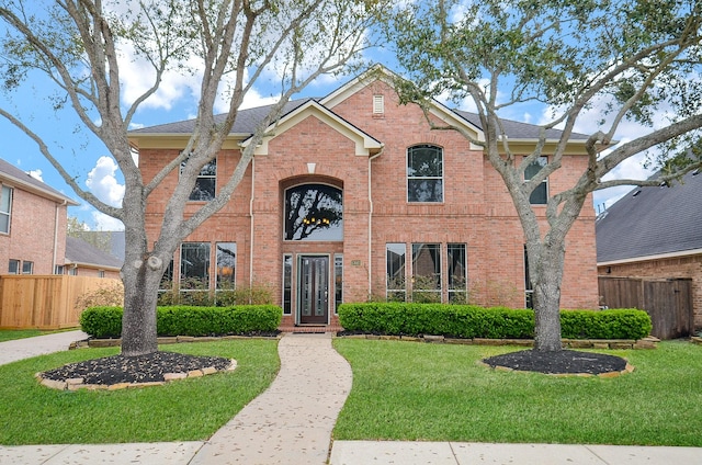 traditional home with brick siding, fence, and a front yard