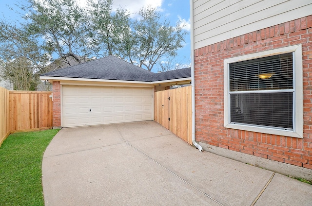 view of home's exterior with driveway, fence, a shingled roof, a garage, and brick siding