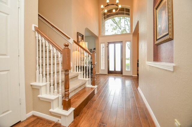 entryway featuring plenty of natural light, a towering ceiling, wood-type flooring, and a chandelier