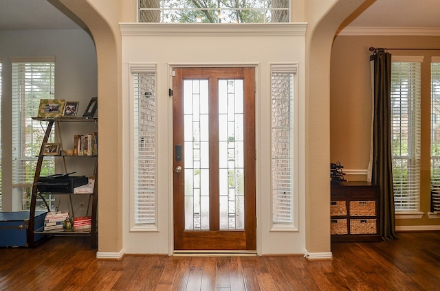 entrance foyer with arched walkways, ornamental molding, and hardwood / wood-style floors