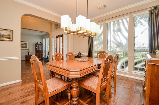 dining space featuring a healthy amount of sunlight, visible vents, arched walkways, ornamental molding, and light wood-type flooring