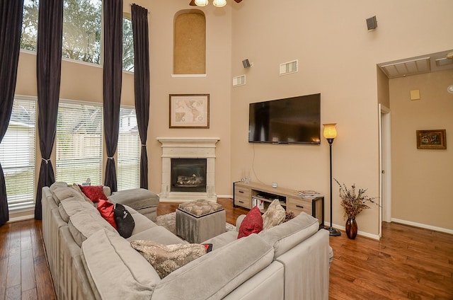 living area with visible vents, a high ceiling, a glass covered fireplace, and wood-type flooring