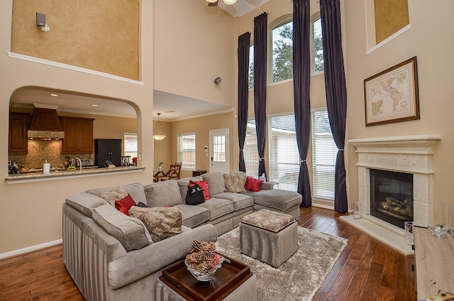 living area featuring ornamental molding, dark wood-style flooring, a towering ceiling, a glass covered fireplace, and baseboards