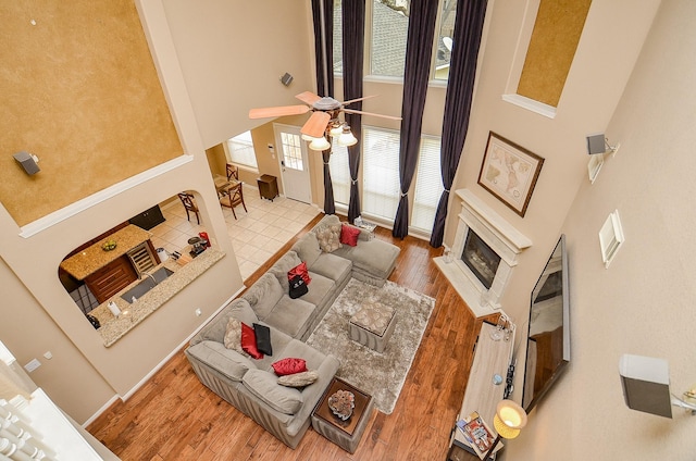 living area with a ceiling fan, wood finished floors, a fireplace, baseboards, and a towering ceiling