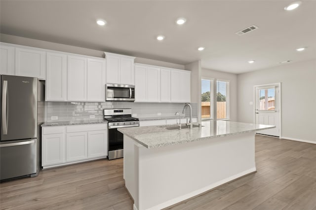 kitchen featuring visible vents, a kitchen island with sink, a sink, stainless steel appliances, and white cabinetry