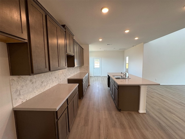 19127 Hazel Firs Ln, Magnolia, TX 77355 - kitchen featuring dark brown cabinetry, light wood-style flooring, decorative backsplash, a kitchen island with sink, and a sink