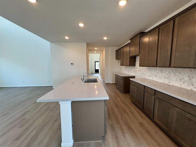 19127 Hazel Firs Ln, Magnolia, TX 77355 - kitchen featuring a sink, light wood-style floors, dark brown cabinetry, decorative backsplash, and baseboards