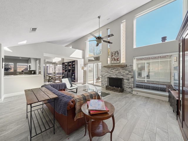 living area with a ceiling fan, baseboards, visible vents, a fireplace, and a textured ceiling