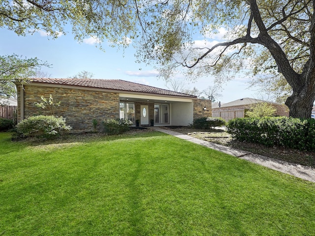 rear view of property featuring stone siding, a lawn, a tiled roof, and fence