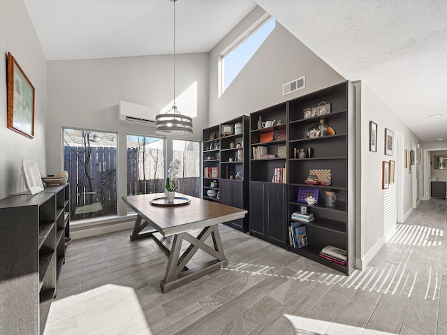 office area with a wall mounted air conditioner, visible vents, high vaulted ceiling, baseboards, and wood tiled floor