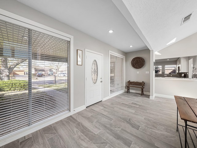 entryway featuring baseboards, visible vents, vaulted ceiling, light wood-style floors, and a textured ceiling