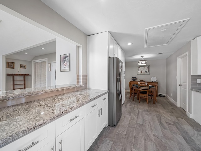 kitchen featuring stainless steel refrigerator with ice dispenser, light stone counters, white cabinetry, recessed lighting, and baseboards