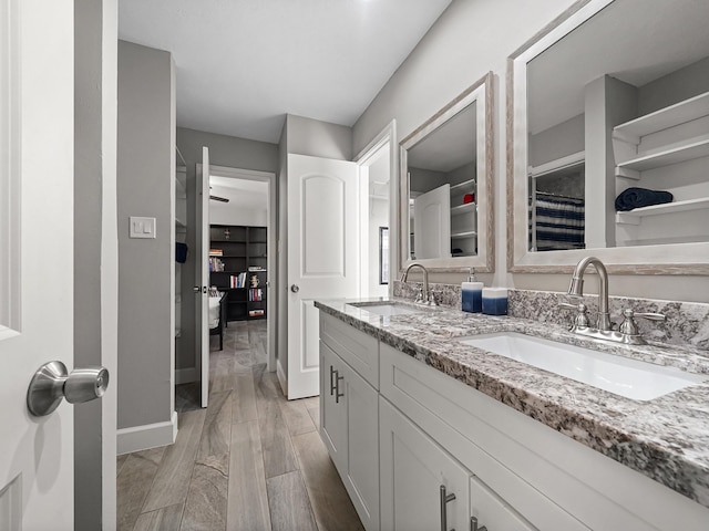 bathroom with double vanity, wood finished floors, baseboards, and a sink