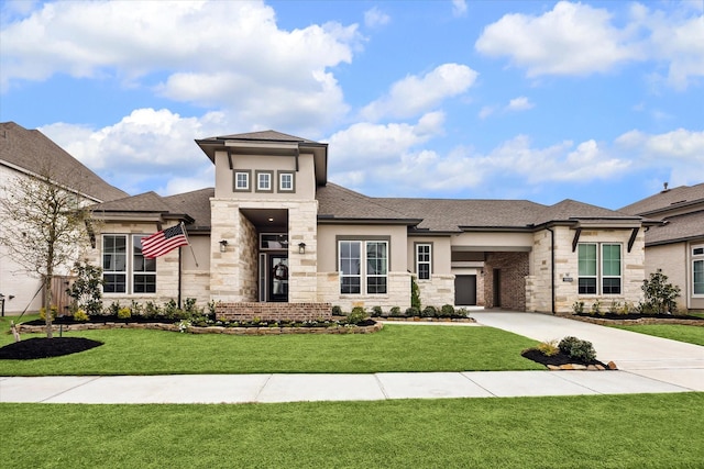 prairie-style house with stucco siding, driveway, stone siding, roof with shingles, and a front yard