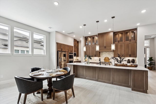 kitchen with tasteful backsplash, glass insert cabinets, light countertops, hanging light fixtures, and stainless steel fridge