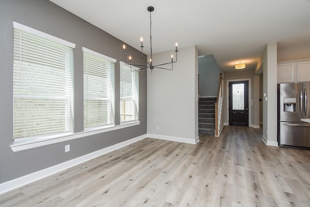 unfurnished dining area with light wood finished floors, a chandelier, stairs, and baseboards