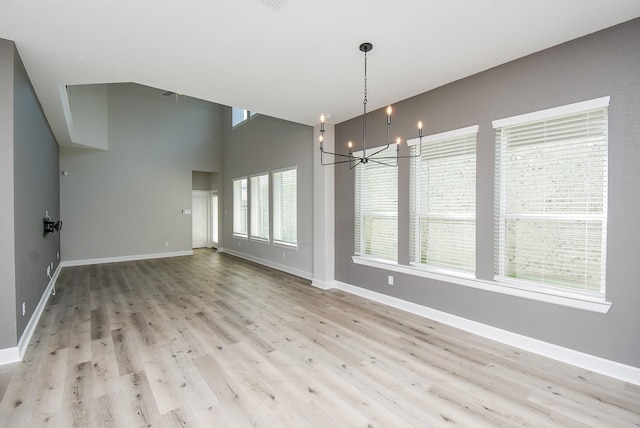 unfurnished dining area featuring light wood-type flooring, baseboards, a chandelier, and a towering ceiling