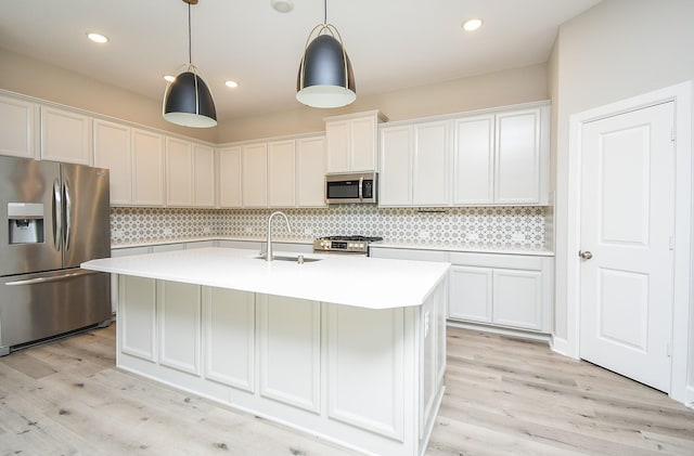 kitchen featuring light wood finished floors, light countertops, decorative backsplash, stainless steel appliances, and a sink