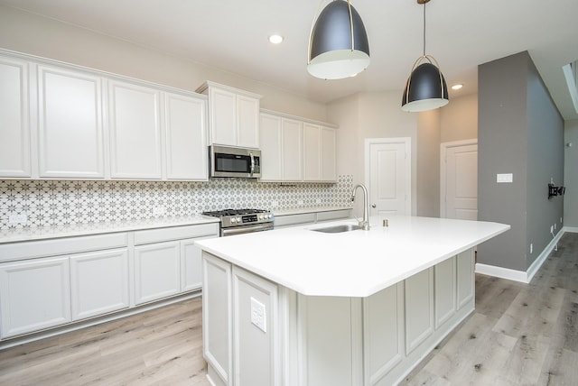 kitchen with backsplash, a center island with sink, appliances with stainless steel finishes, light wood-style floors, and a sink