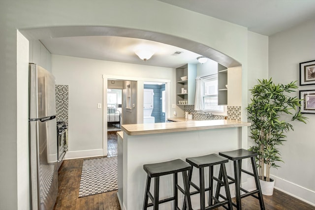 kitchen featuring arched walkways, open shelves, freestanding refrigerator, and dark wood-style flooring