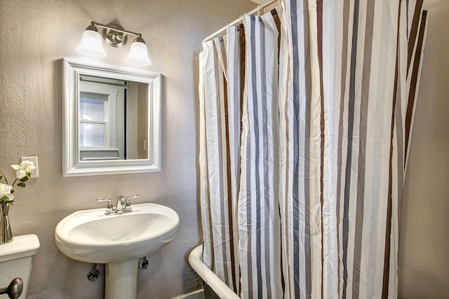 bathroom featuring toilet, shower / bath combo, and a textured wall