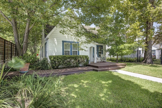 view of property hidden behind natural elements with a wooden deck, a front lawn, and fence