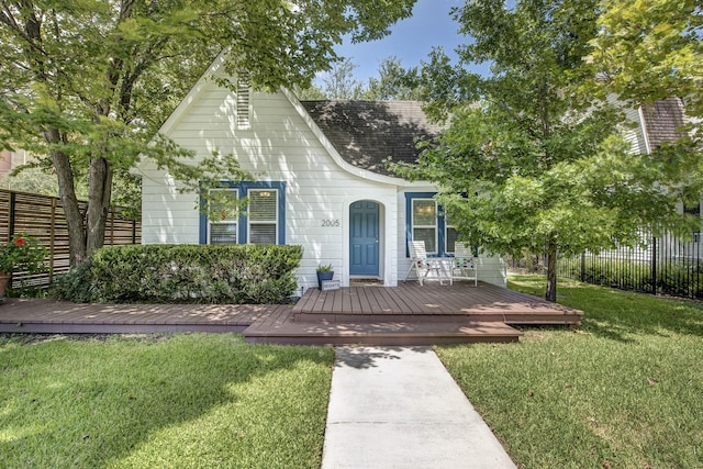 view of front of property featuring a front yard, fence, roof with shingles, and a wooden deck