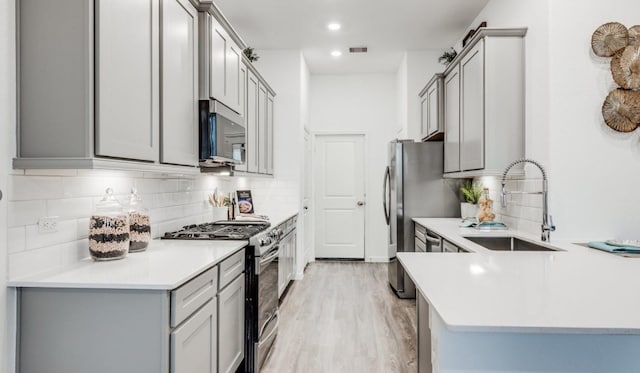 kitchen featuring light wood finished floors, gray cabinets, a sink, stainless steel appliances, and light countertops