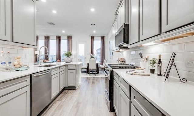 kitchen with a sink, light wood-type flooring, appliances with stainless steel finishes, and light countertops