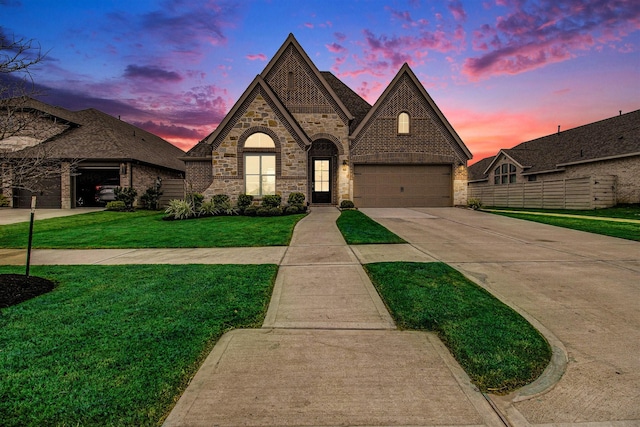 french provincial home featuring brick siding, fence, concrete driveway, a lawn, and a garage