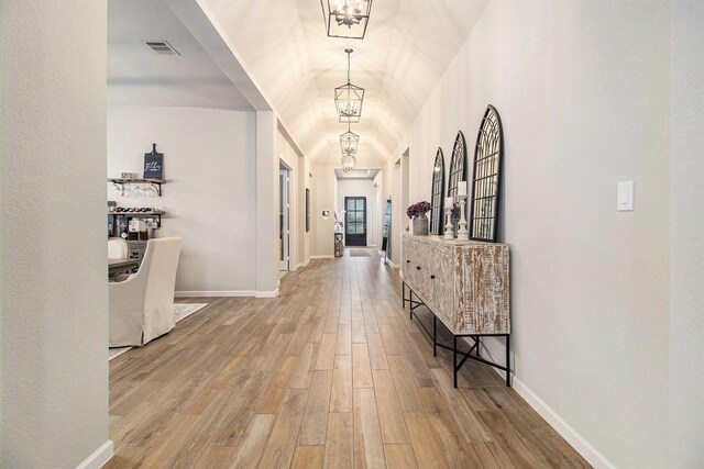 corridor featuring a chandelier, visible vents, baseboards, and wood finished floors