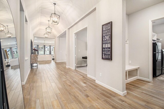 entrance foyer with light wood-style flooring, ceiling fan with notable chandelier, lofted ceiling, and baseboards