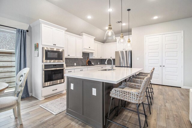 kitchen featuring light wood finished floors, visible vents, backsplash, stainless steel appliances, and a sink