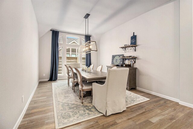 dining room featuring an inviting chandelier, lofted ceiling, wood finished floors, and baseboards