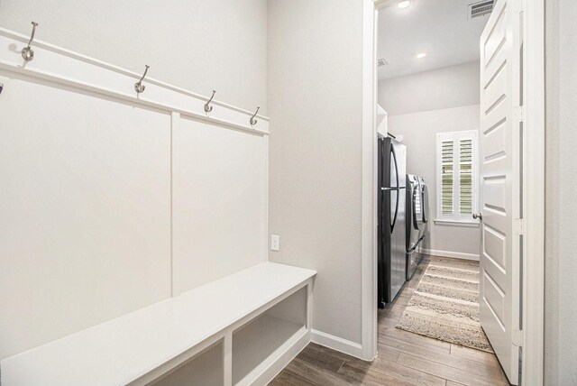 mudroom featuring visible vents, wood finished floors, baseboards, and washing machine and dryer