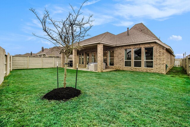 back of property with brick siding, a shingled roof, a yard, a fenced backyard, and a patio