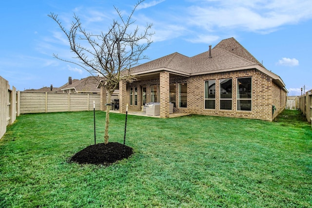 back of property with a lawn, roof with shingles, brick siding, and a fenced backyard