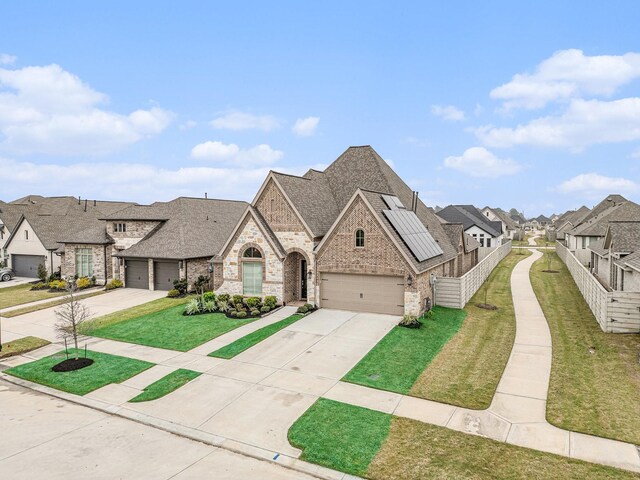 french country home with a front lawn, a residential view, concrete driveway, a garage, and brick siding